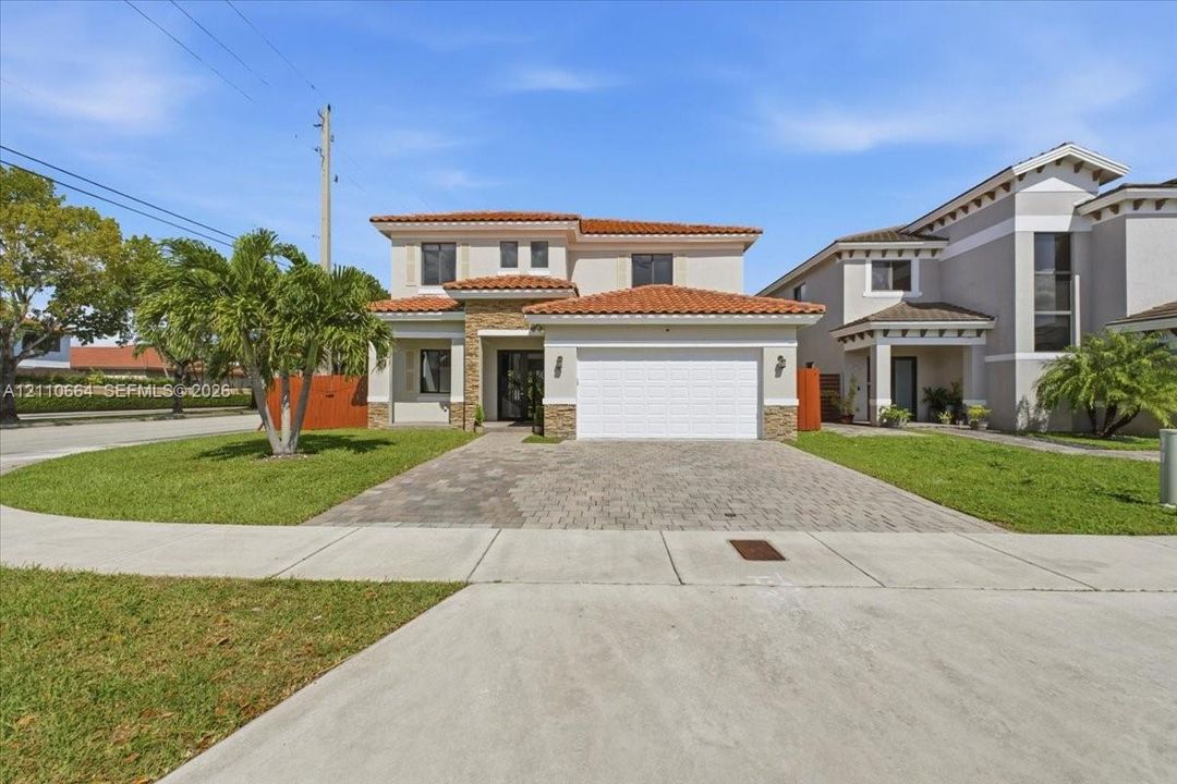 Two-story residence featuring a tile roof, exterior stone veneer accents, a paver driveway and an attached two-car garage