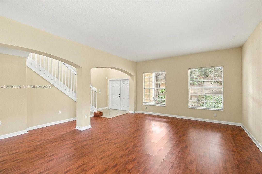 Open-concept room featuring wood-finish flooring, dual arched entryways, double-door front entry, and a staircase with a white balustrade
