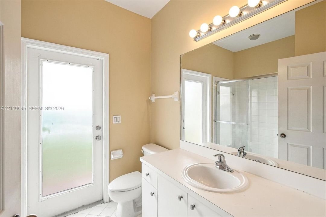 Vanity with a solid-surface countertop and integrated sink, large wall-mounted mirror, multi-bulb vanity light fixture, glass-enclosed shower, and full-lite exterior door with frosted glass