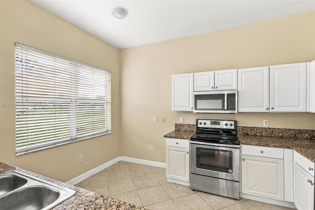 Kitchen featuring white shaker-style cabinetry, stone-finish countertops, stainless steel electric range, built-in microwave, and tile flooring