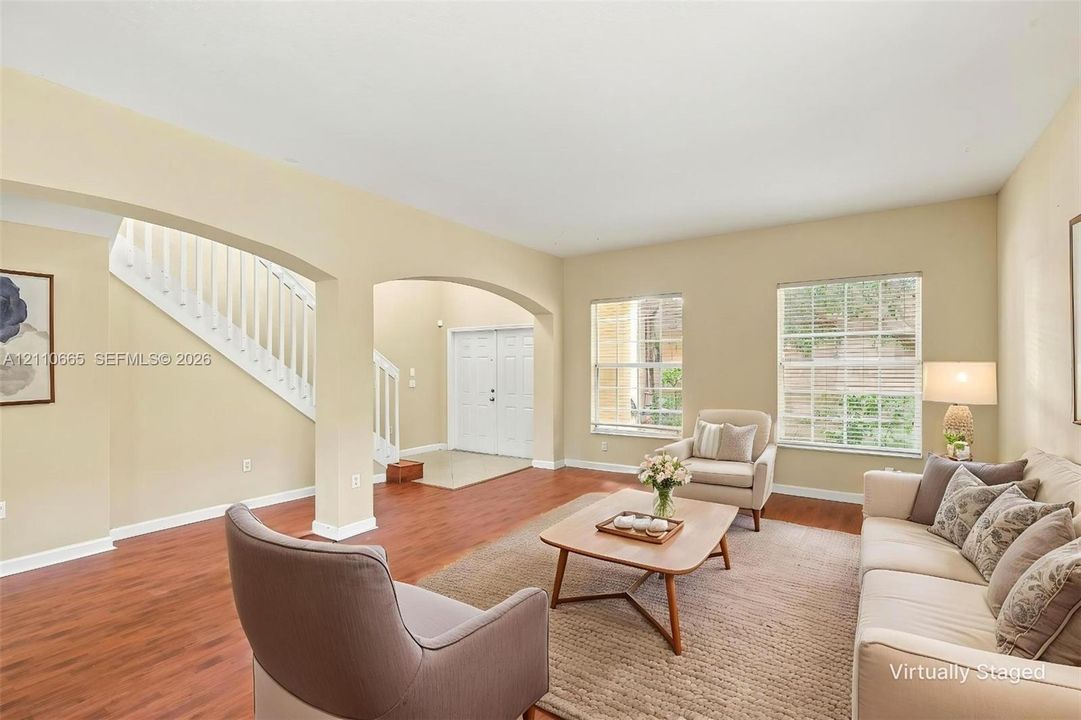 Living area featuring wood-finish flooring, white staircase with balusters, arched architectural openings, and dual pane windows