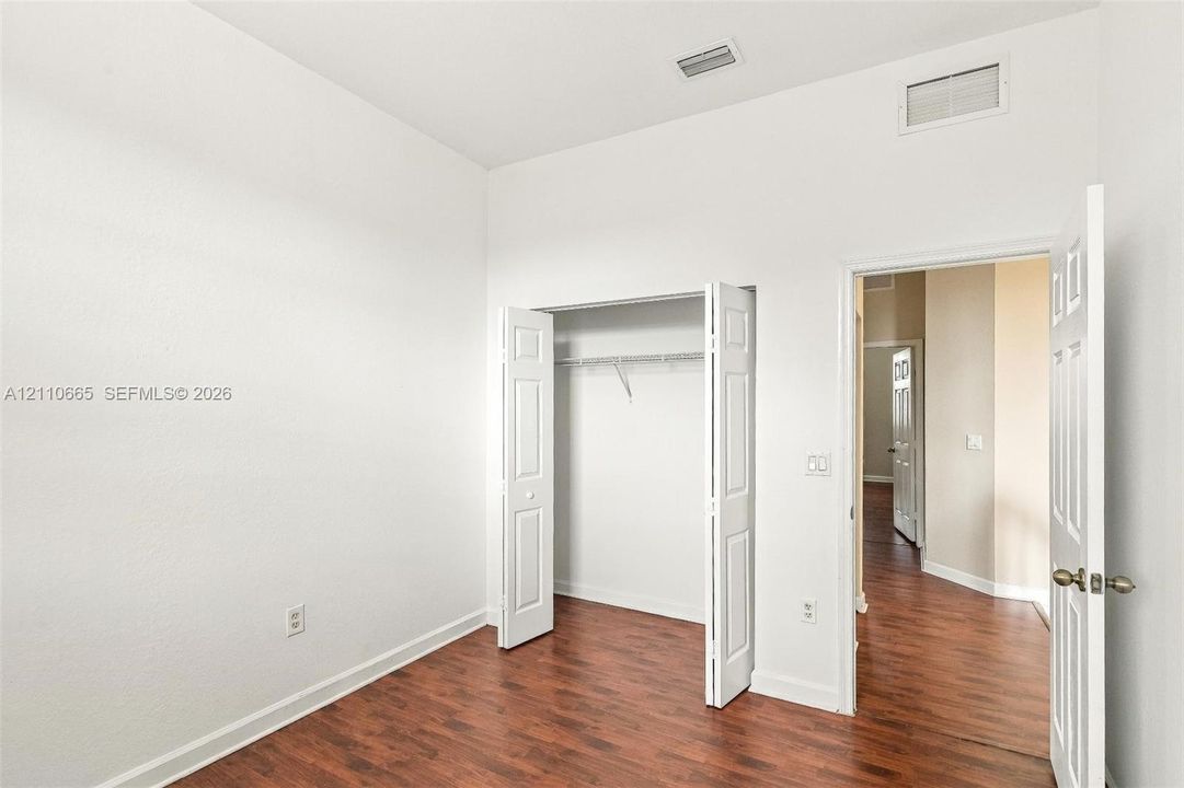 Room featuring high ceilings, wood-finish flooring, and a walk-in closet with integrated shelving