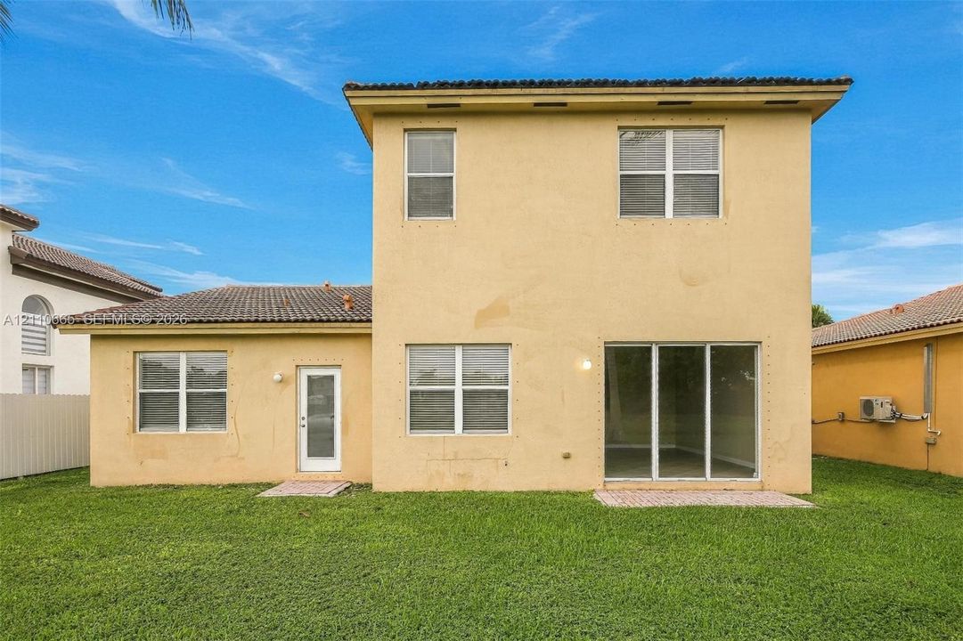 Two-story exterior featuring a stucco facade, a tile roof, a large sliding glass door, multiple double-hung windows, and a rear lawn area