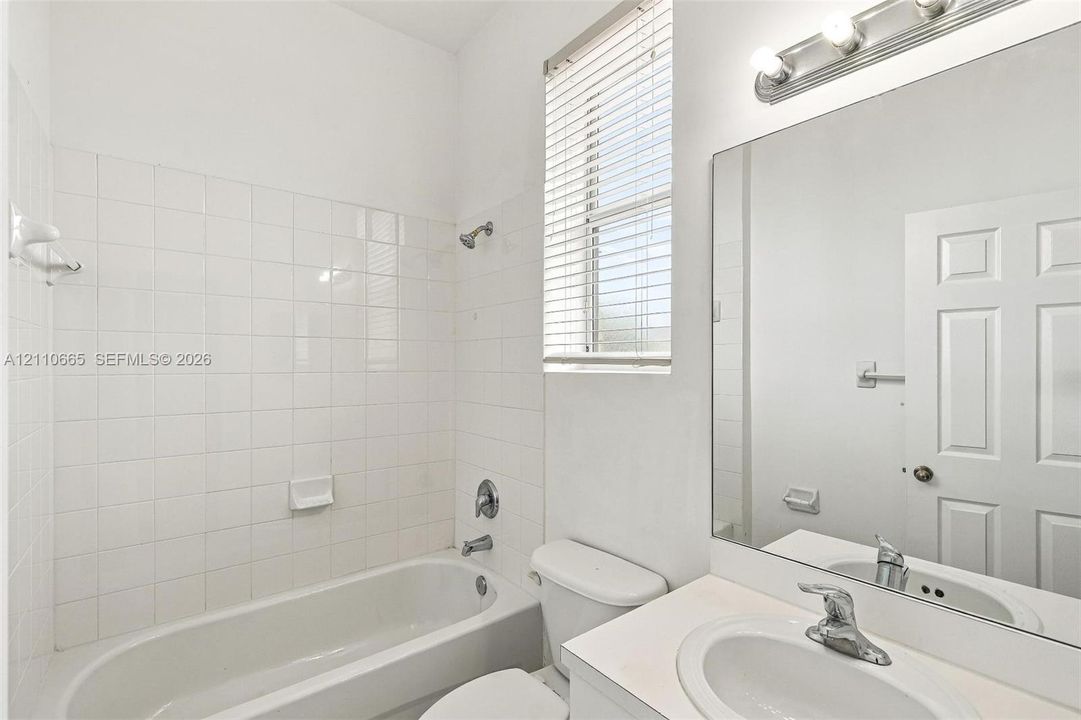 Bathroom featuring a white bathtub, white square wall tile surround, vanity with an integrated sink, large wall-mounted mirror, and multi-bulb vanity light fixture