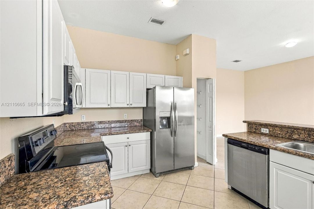 Kitchen featuring white cabinetry, stone-finish countertops, stainless steel appliances, and ceramic tile flooring