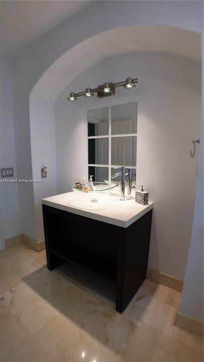 Vanity featuring a dark wood-finish base, neutral countertop, and a clear glass vessel sink with a polished metal faucet