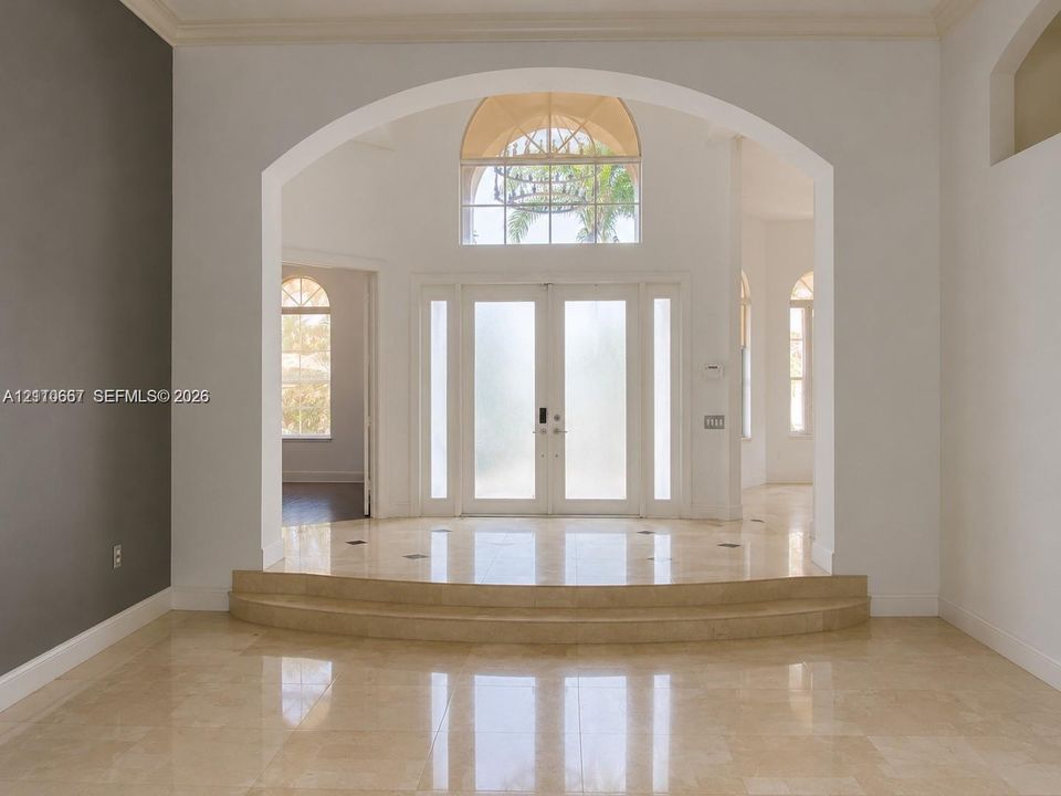 Entryway featuring stone tile flooring, a two-step raised landing, a vaulted arched entryway, double-door entry with sidelights, and an arched transom window