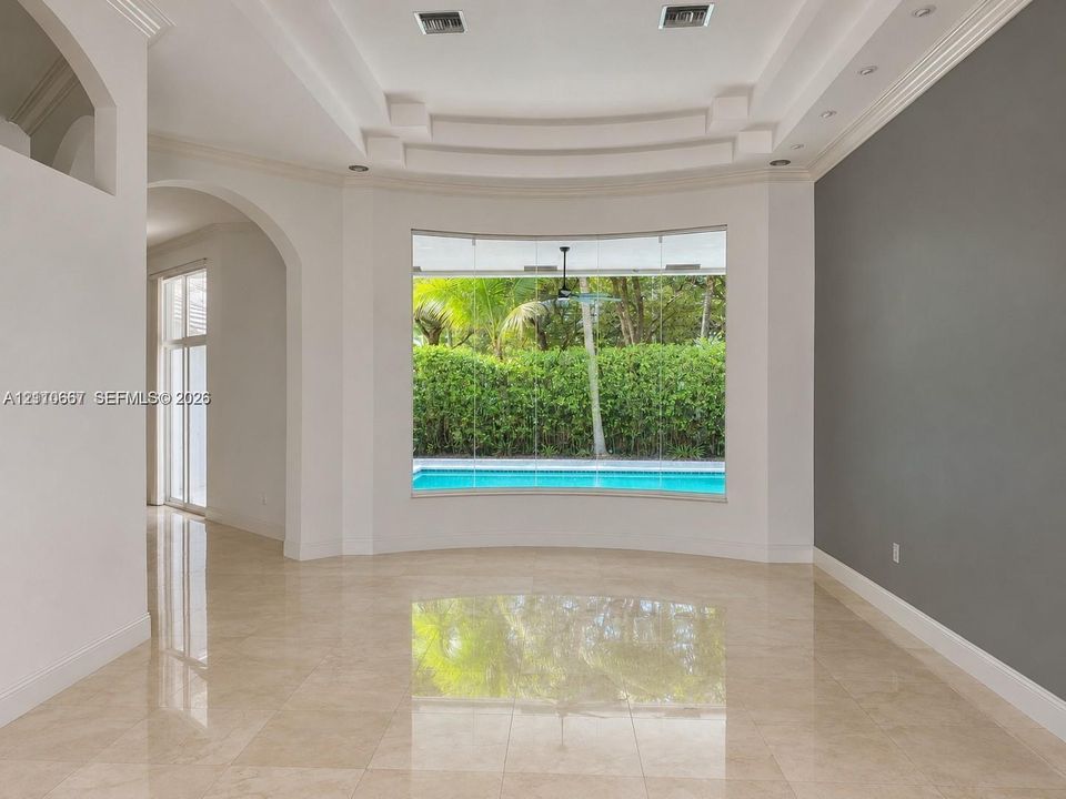 Living area featuring polished tile flooring, a recessed tray ceiling with integrated lighting, and a floor-to-ceiling picture window overlooking a swimming pool and greenery