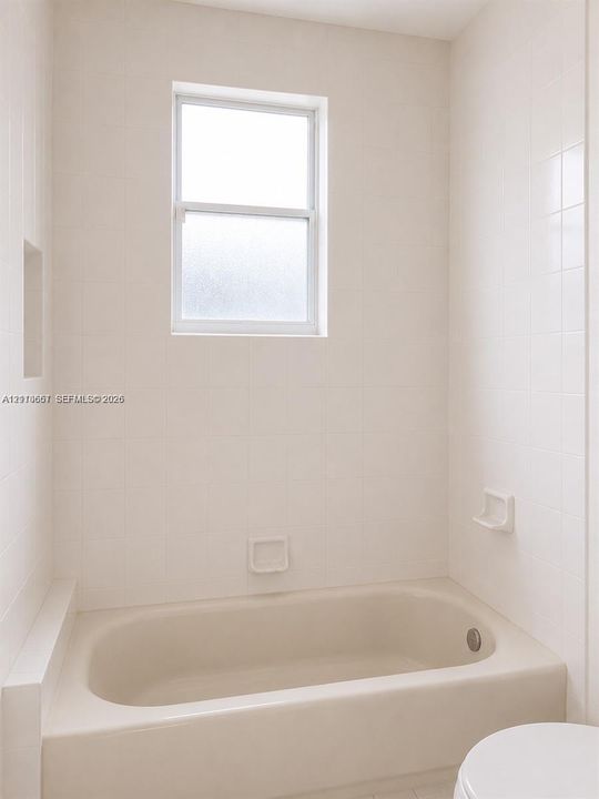 Bathtub with a shower surround featuring white tile wall cladding, an inset soap niche, and a single-hung window