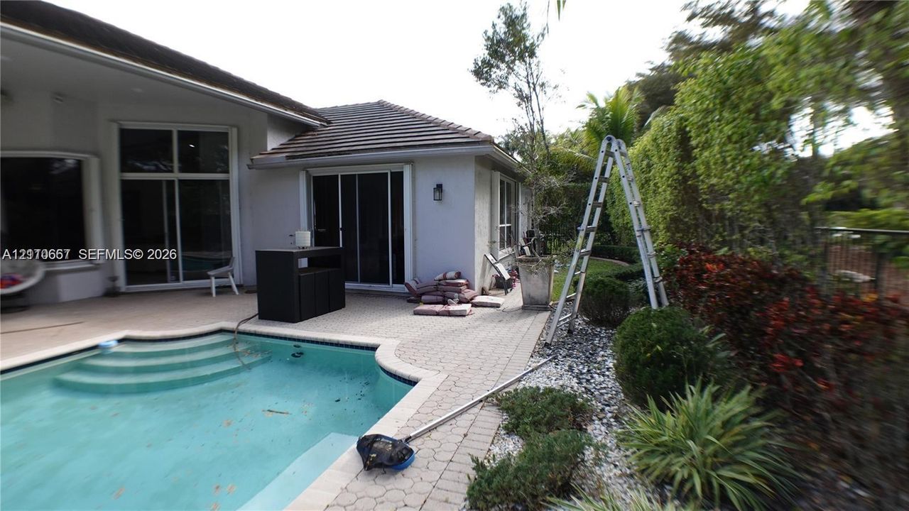 Rear patio featuring concrete paver decking, swimming pool with integrated stairs, and exterior wall-mounted lighting