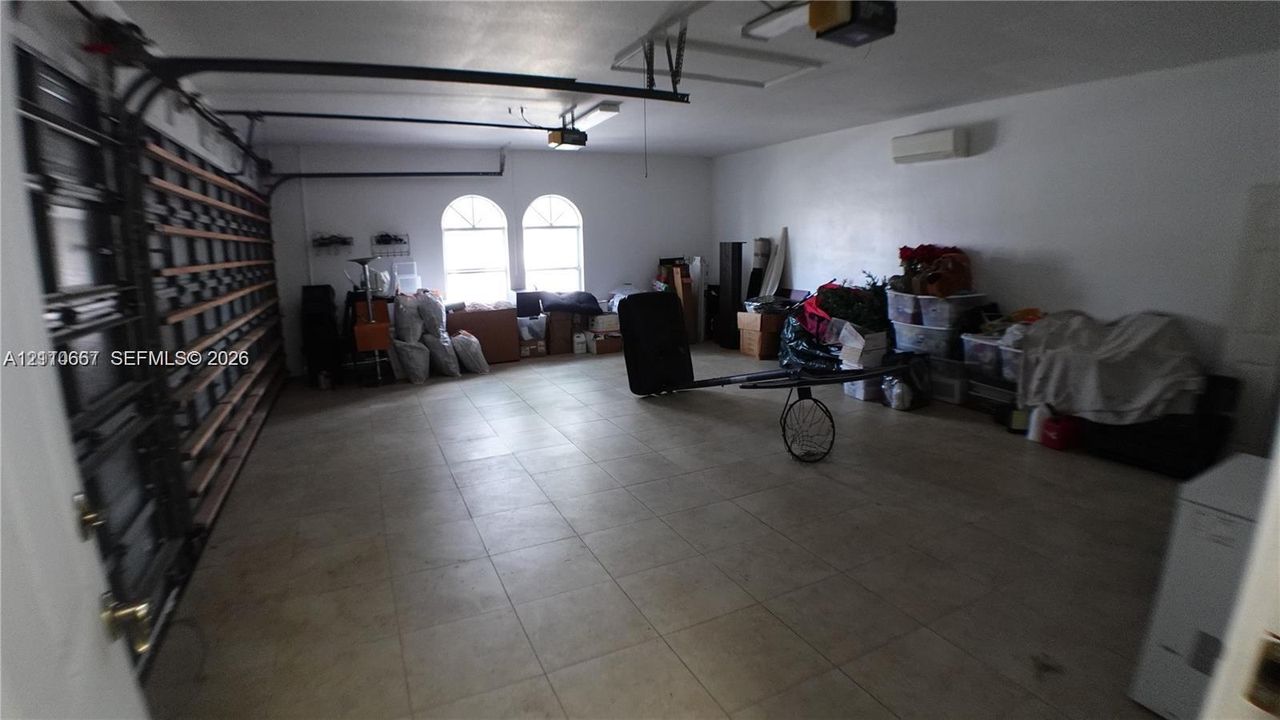Attached garage featuring tile flooring, arched windows, wall-mounted climate control unit, and extensive built-in wall shelving