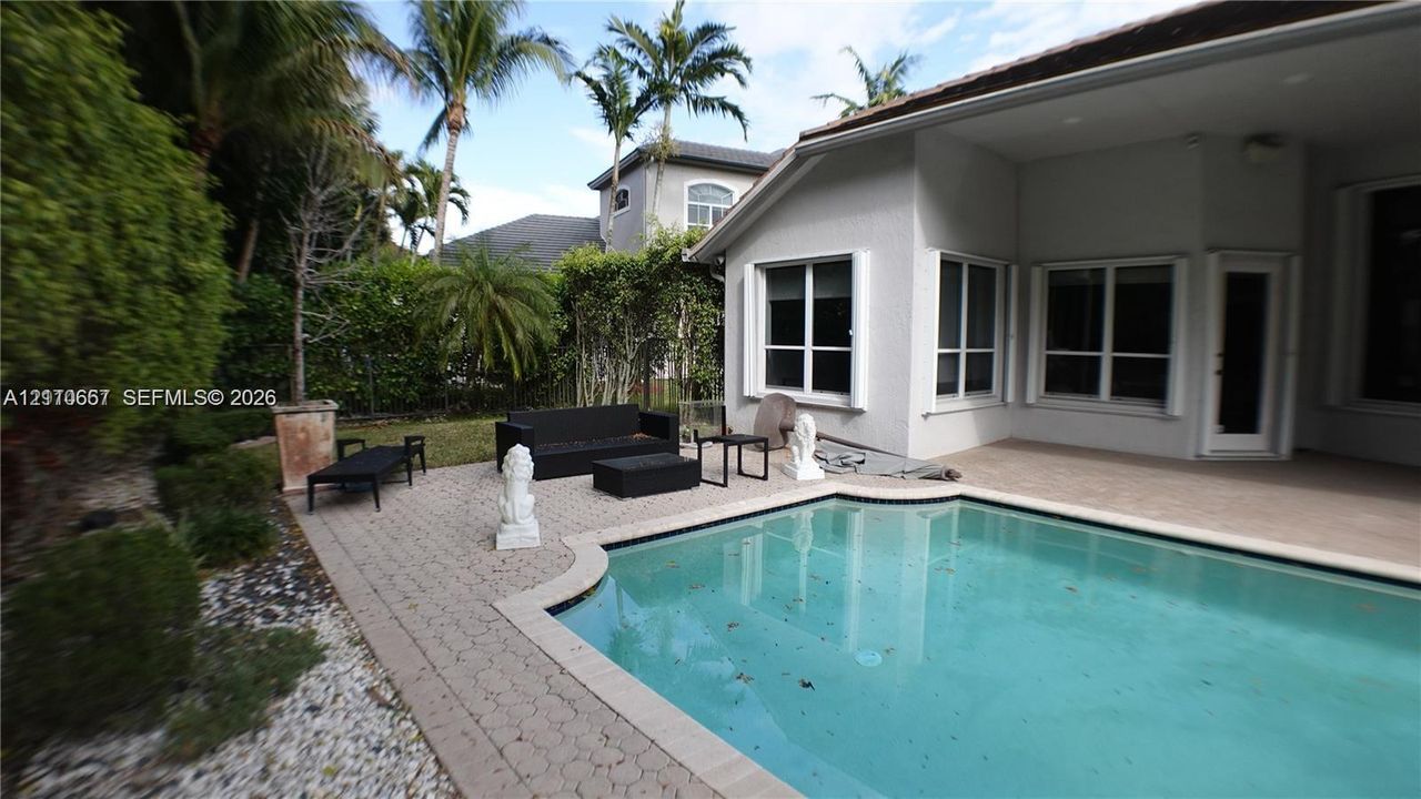 In-ground swimming pool featuring a paver patio, covered terrace, exterior lighting fixtures, and landscaped perimeter
