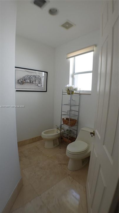 Neutral-toned stone flooring, one-piece dual-flush toilet, bidet, and single-pane window with top-down shade