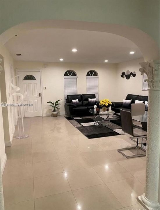 Living space featuring large-format tile flooring, arched entryways, decorative column detailing, recessed lighting, and dual arched windows