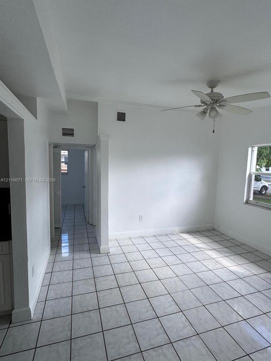 Neutral-toned tile flooring, white-finish walls, ceiling-mounted light fixture with fan, and a single-pane window
