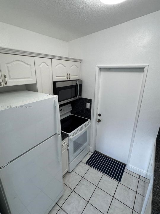Kitchen area featuring white cabinetry, a built-in stainless steel microwave, an electric range, and light-toned floor tiling