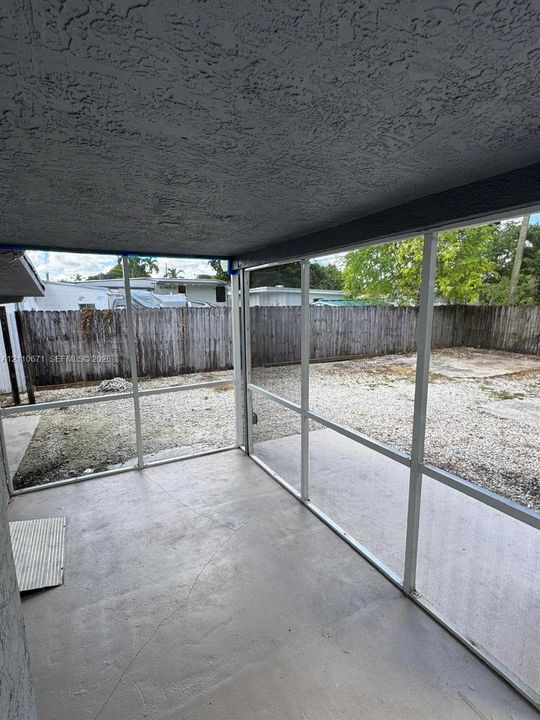 Screened-in enclosure with concrete flooring, textured ceiling, and wood privacy fencing surrounding the rear grounds
