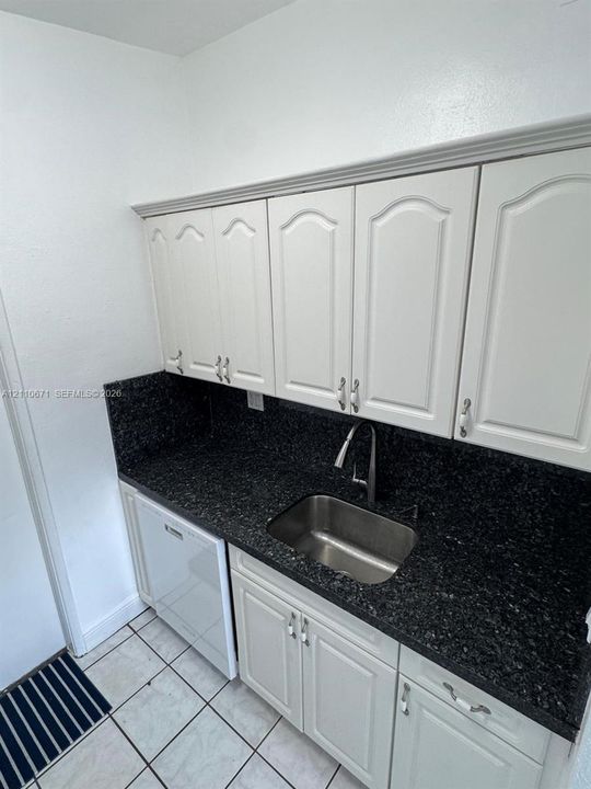 Kitchen area featuring white cabinetry with crown molding, dark stone-finish countertops, stainless steel undermount sink, gooseneck pull-down faucet, and integrated dishwasher