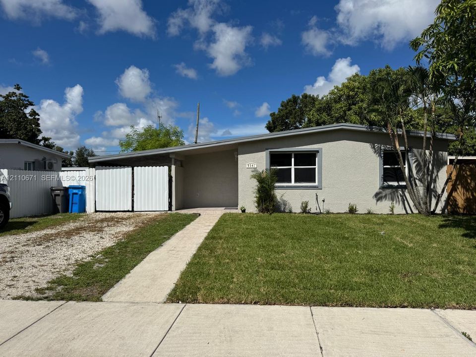 Single-story residence featuring a neutral stucco exterior, low-pitched roofline, front-facing lawn, stone-surfaced driveway, and metal privacy gate