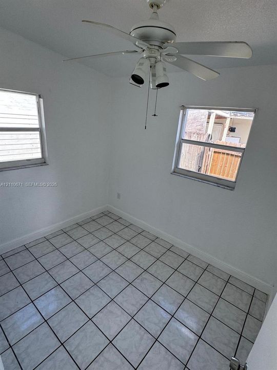 Room featuring white tile flooring, dual windows, and a ceiling-mounted light fixture with a fan