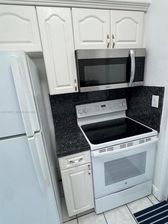 Kitchen featuring white cabinetry, dark stone countertops, built-in stainless steel microwave, electric range, and white refrigerator