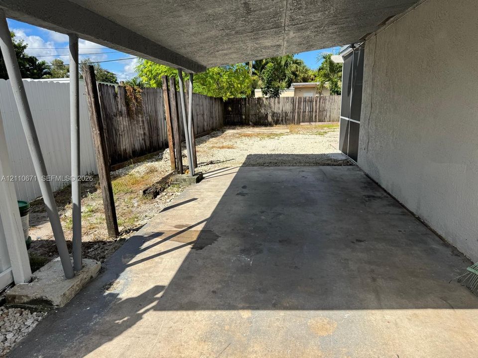 Covered concrete patio with metal support pillars, wood-fencing perimeter, and white vinyl privacy screening