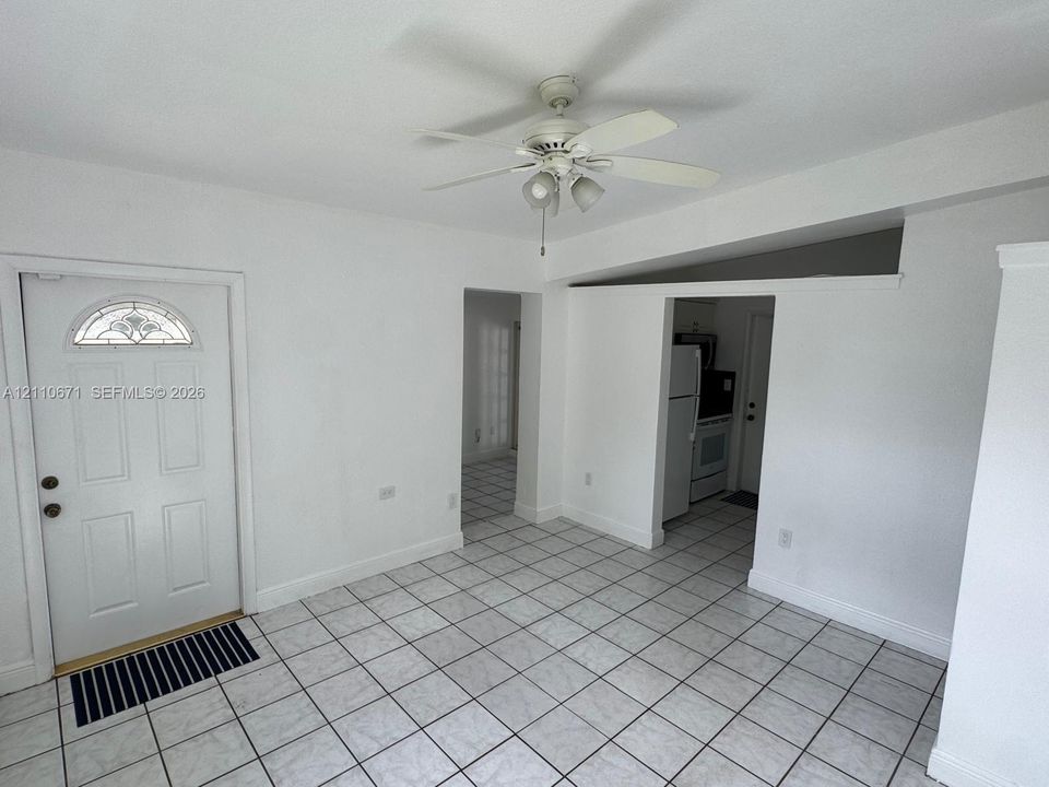 Interior area featuring tile flooring, a white paneled entry door with a decorative glass insert, a sloped ceiling, and a ceiling fan with integrated lighting