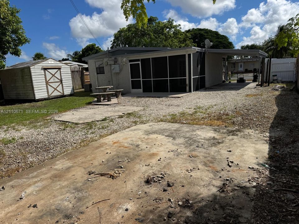Rear exterior featuring a screened-in porch, metal storage shed, gravel yard, and attached carport