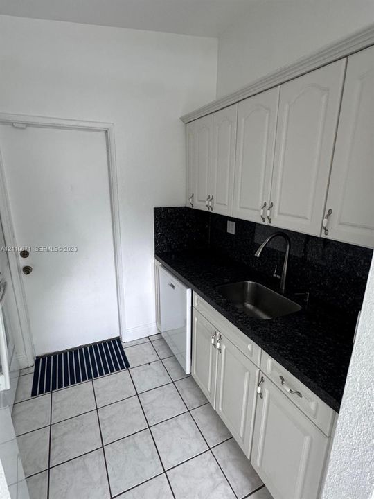 Kitchen featuring off-white cabinetry, dark stone-style countertops, stainless steel undermount sink with arched faucet, and tiled flooring