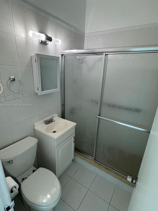 Bathroom featuring a white vanity cabinet with an integrated sink, shower enclosure with textured glass sliding doors, wall-mounted medicine cabinet, and tiled flooring