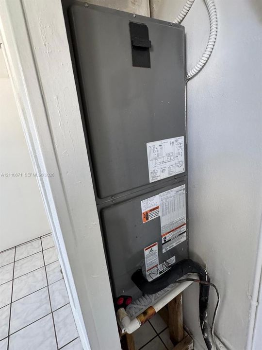 Vertical HVAC air handler unit featuring a metallic exterior finish, integrated electrical conduit, and exposed piping connections