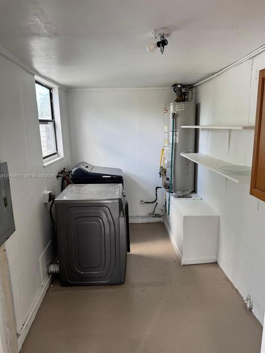Utility space featuring built-in wall shelving, a designated water heater platform, and a window for natural light