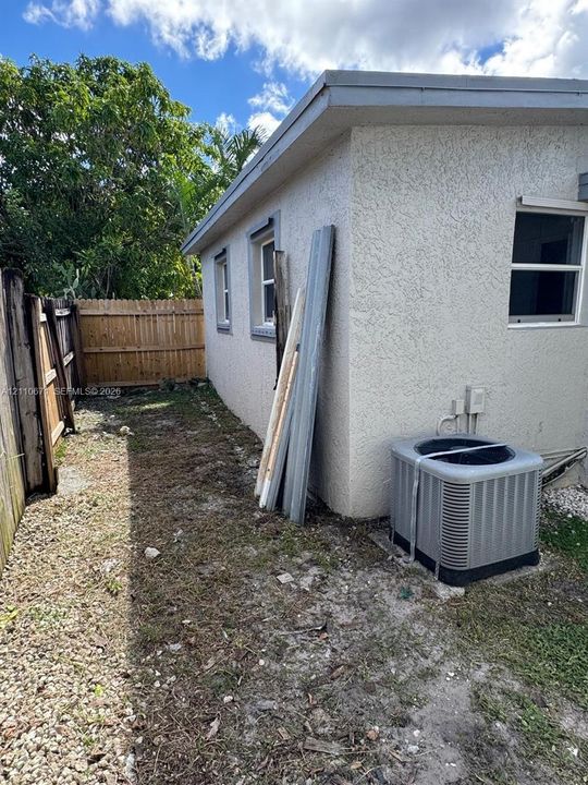 Exterior side yard featuring a stucco finish, external HVAC unit, and wooden perimeter fencing