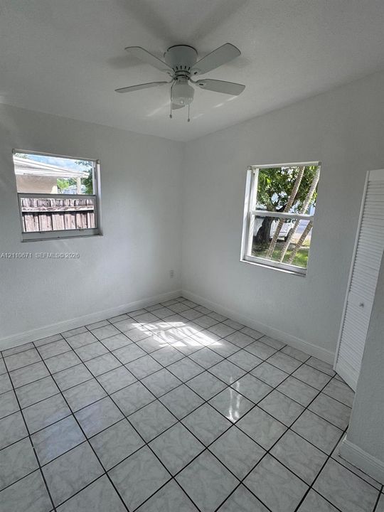 Neutral-toned interior room featuring tile flooring, dual windows, a ceiling fan, and a built-in louvered closet door