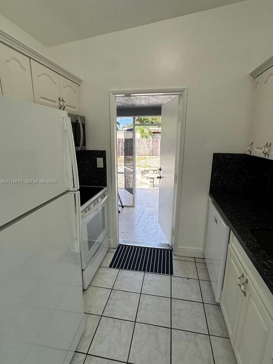 Kitchen featuring white cabinetry, dark stone-finish countertops, tile flooring, and white appliances including a range and refrigerator