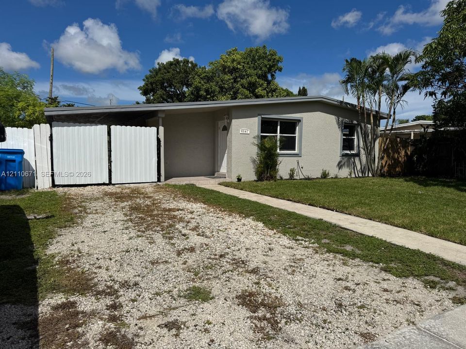 Single-story residence featuring a neutral stucco exterior, low-pitch roofline, front-facing covered carport, and enclosed white privacy fencing