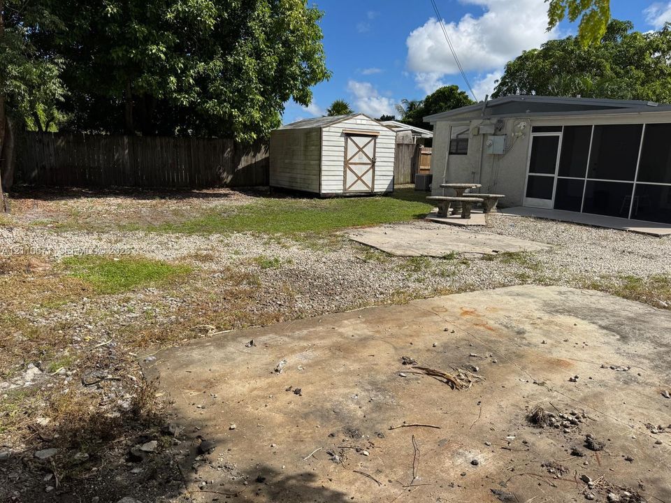 Backyard featuring a concrete patio, stone ground cover, detached storage shed, and a screened-in enclosure