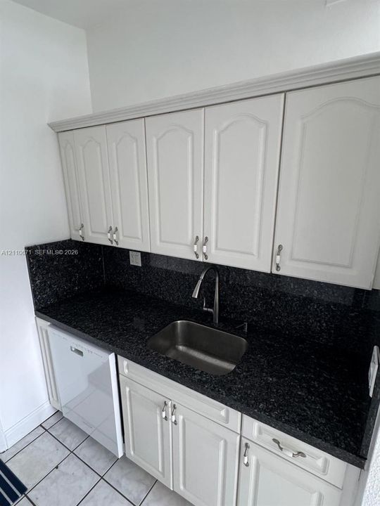 Kitchen featuring white raised-panel cabinetry, dark stone countertops, integrated dishwasher, stainless steel undermount sink, and high-arc faucet