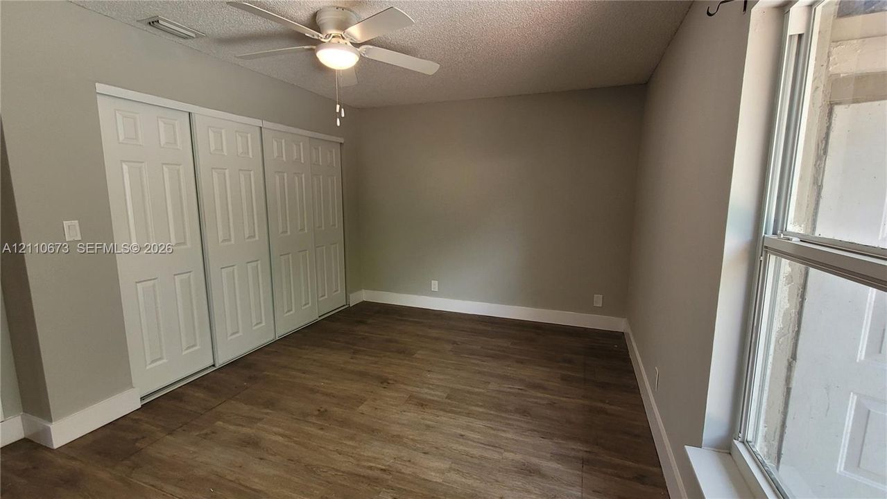 Wood-finish flooring, multi-panel sliding closet doors, ceiling fan with integrated light fixture, and large window with natural lighting
