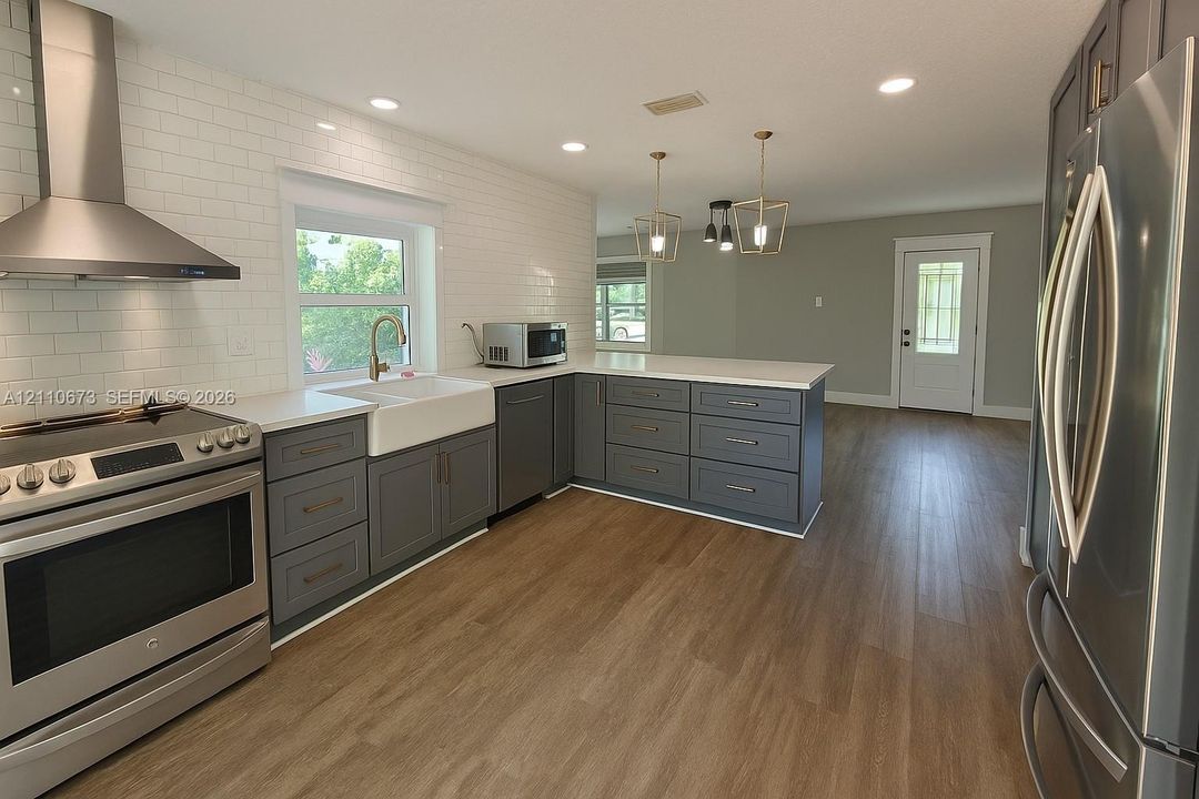 Kitchen featuring gray cabinetry, stainless steel appliances, white subway tile backsplash, white countertops, and wood-finish flooring