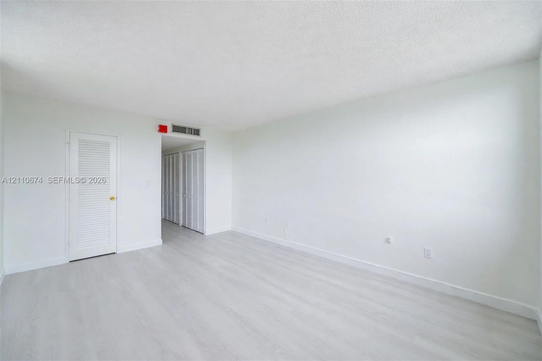 Neutral-toned room featuring wood-finish flooring, white walls, and closet doors with louvered panels