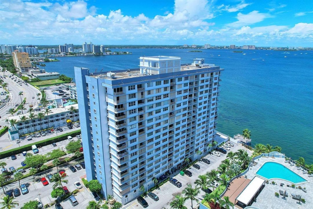 High-rise residential building featuring a concrete exterior, private balconies, an on-site swimming pool, and dedicated parking, situated along a waterfront coastline