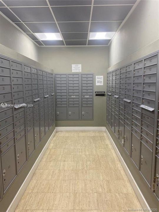 Mail center featuring wall-mounted metal mailboxes, grid-patterned drop ceiling, and neutral tile flooring