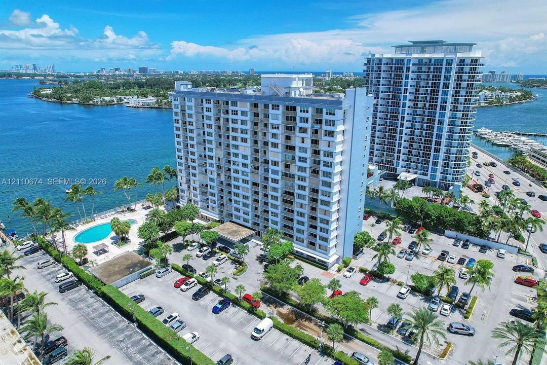 High-rise residential building featuring waterfront positioning, an outdoor swimming pool, landscaped grounds, and surface parking