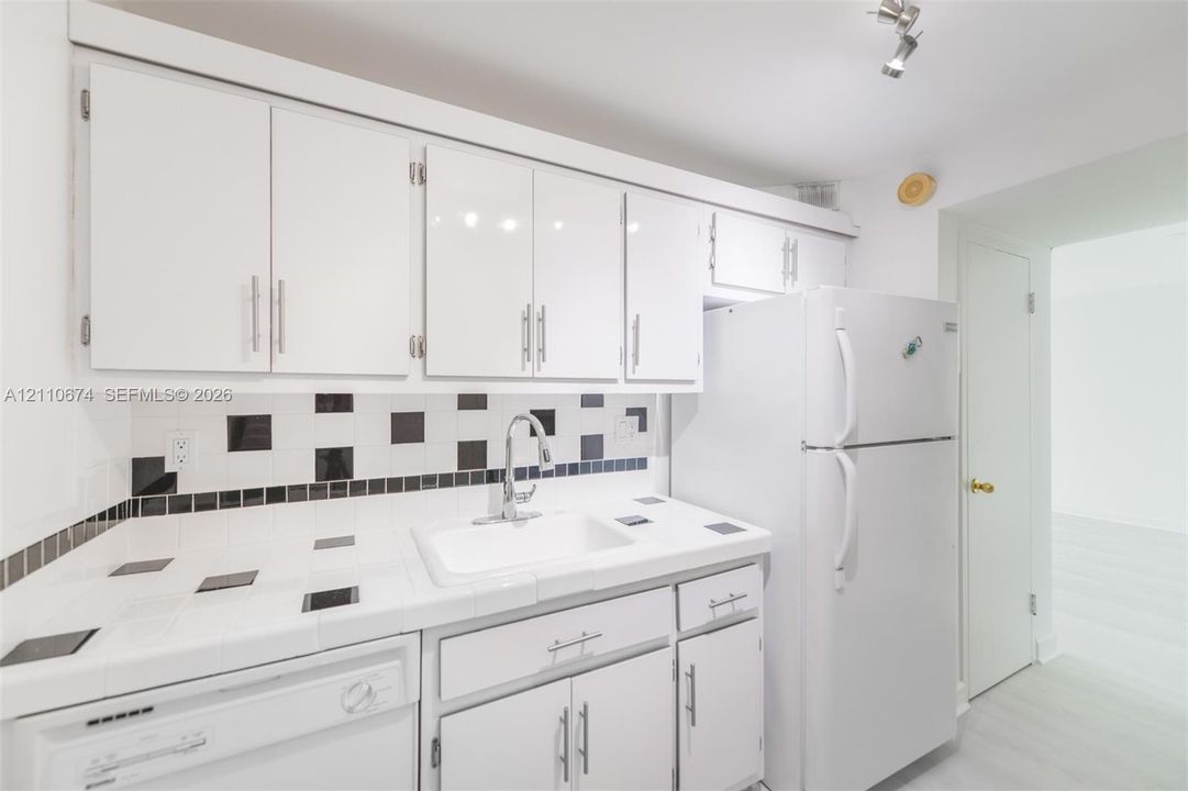 Kitchen featuring white cabinetry with metallic pulls, white tile countertops, geometric tile backsplash, undermount sink with arched faucet, and top-mount track lighting