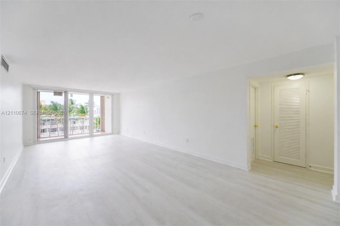 Open interior space featuring light-toned wood-finish flooring, floor-to-ceiling glass sliding doors, and a louvered bi-fold closet door