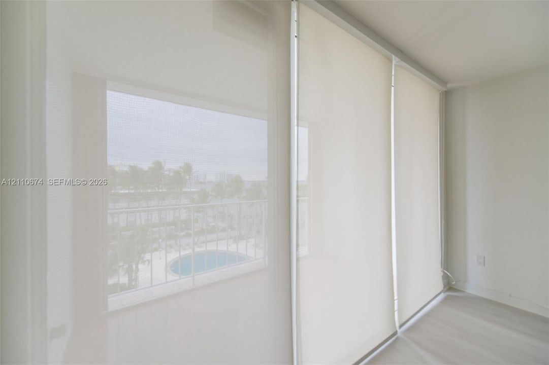 Floor-to-ceiling sliding glass panels featuring neutral roller shades and an exterior metal balcony railing