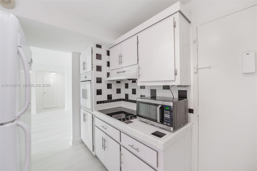 Kitchen featuring white cabinetry, a built-in oven, a black and white geometric backsplash, and light-toned flooring