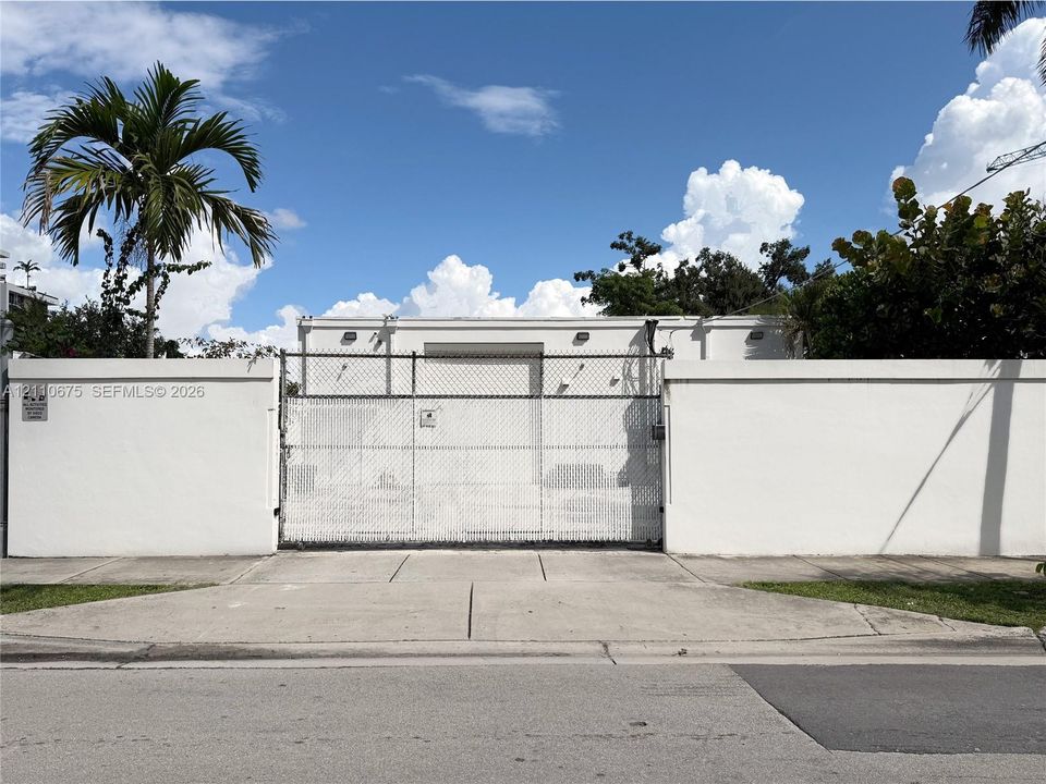 Exterior property frontage featuring a solid perimeter wall, gated chain-link entry, and concrete driveway