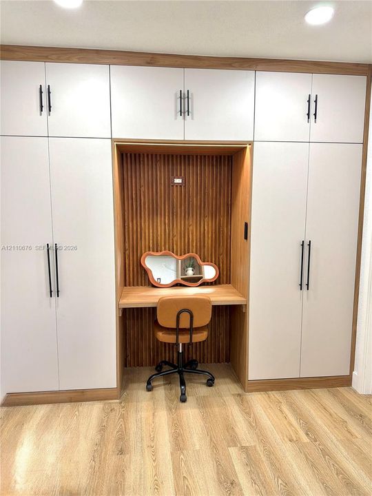 Built-in floor-to-ceiling cabinetry with matte black hardware, integrated wooden desk niche, vertical slat wood-finish wall paneling, and wood-finish flooring